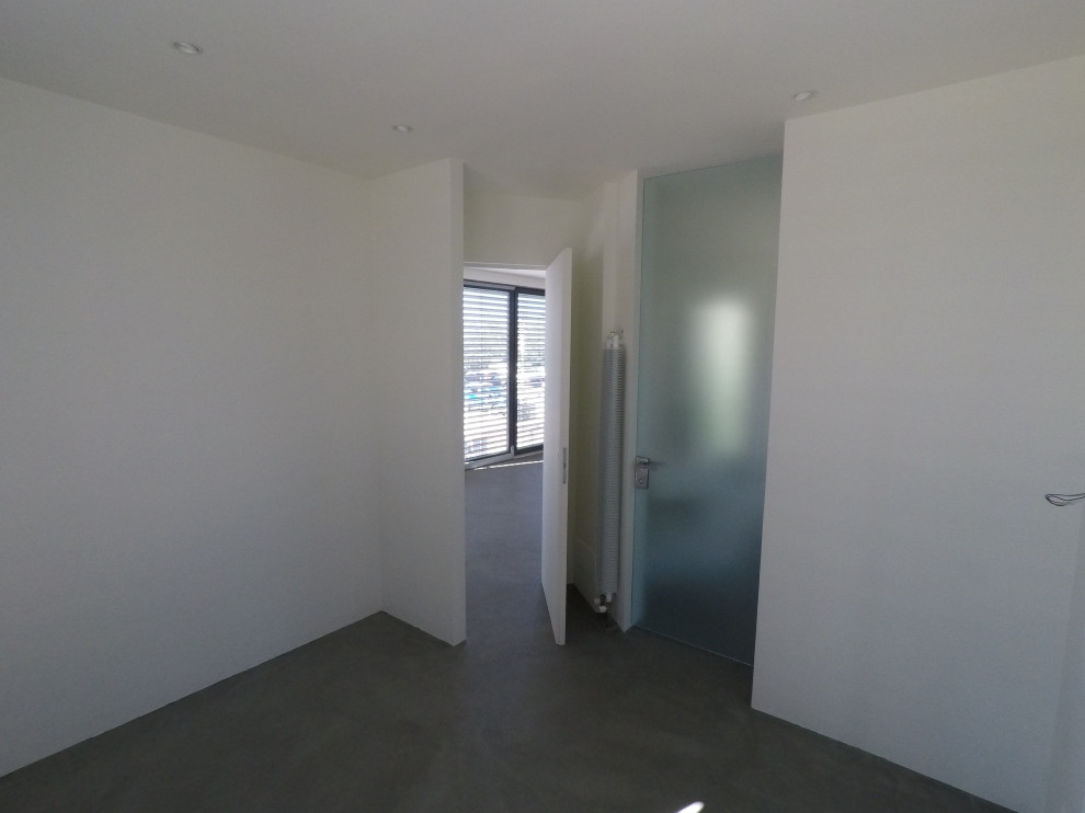 Cette photo montre une petite chambre parentale tendance avec un mur blanc, sol en béton ciré et un sol gris.