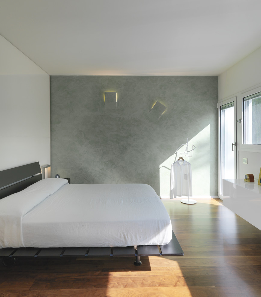 Ejemplo de dormitorio principal actual de tamaño medio sin chimenea con paredes blancas, suelo de madera en tonos medios y suelo marrón