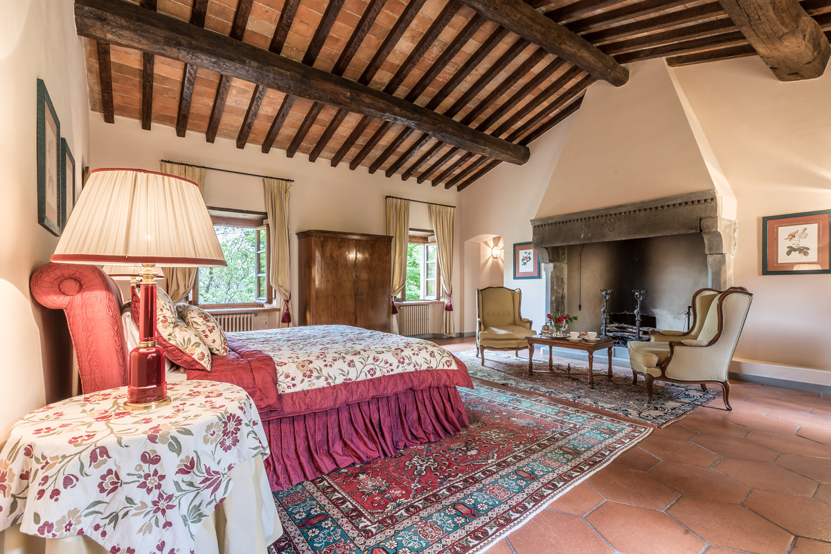 フィレンツェにある巨大なカントリー風のおしゃれな主寝室 (ベージュの壁、テラコッタタイルの床、標準型暖炉、石材の暖炉まわり、赤い床) のインテリア