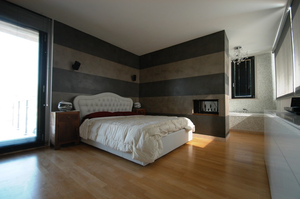 他の地域にある中くらいなコンテンポラリースタイルのおしゃれな主寝室 (マルチカラーの壁、淡色無垢フローリング、両方向型暖炉、漆喰の暖炉まわり、茶色い床) のインテリア