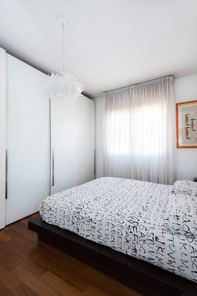 Aménagement d'une chambre parentale moderne avec un mur blanc, un sol en bois brun et aucune cheminée.