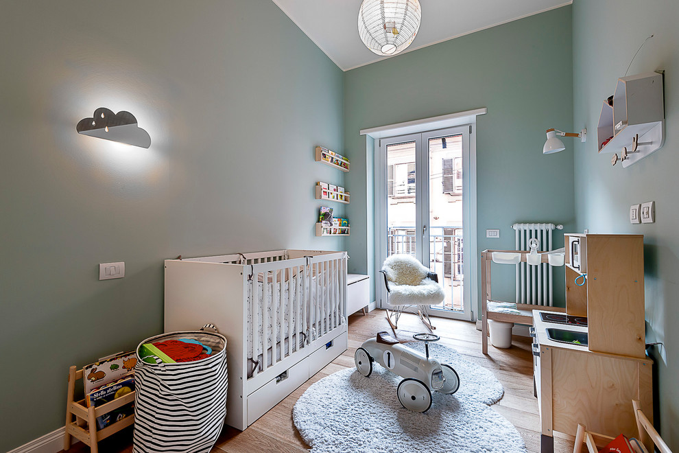 Aménagement d'une chambre de bébé neutre scandinave avec un mur vert et un sol en bois brun.