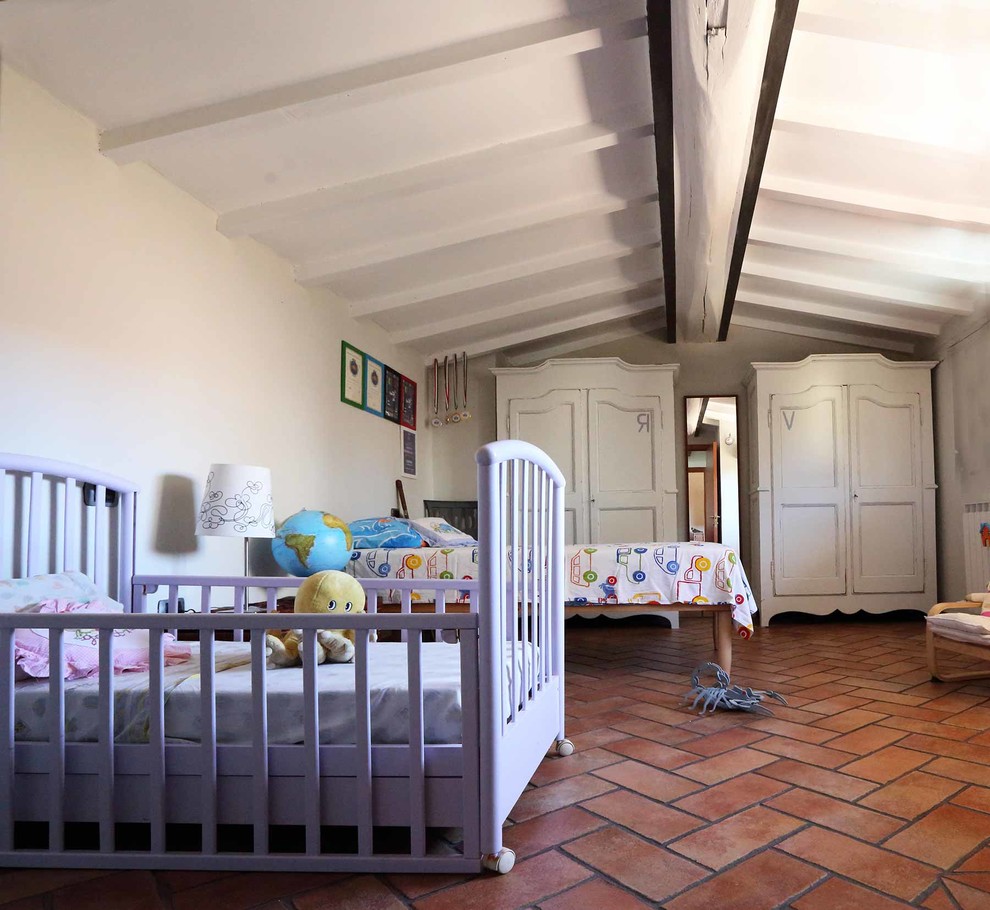 На фото: нейтральная детская среднего размера в стиле кантри с спальным местом, белыми стенами и полом из терракотовой плитки для ребенка от 1 до 3 лет с