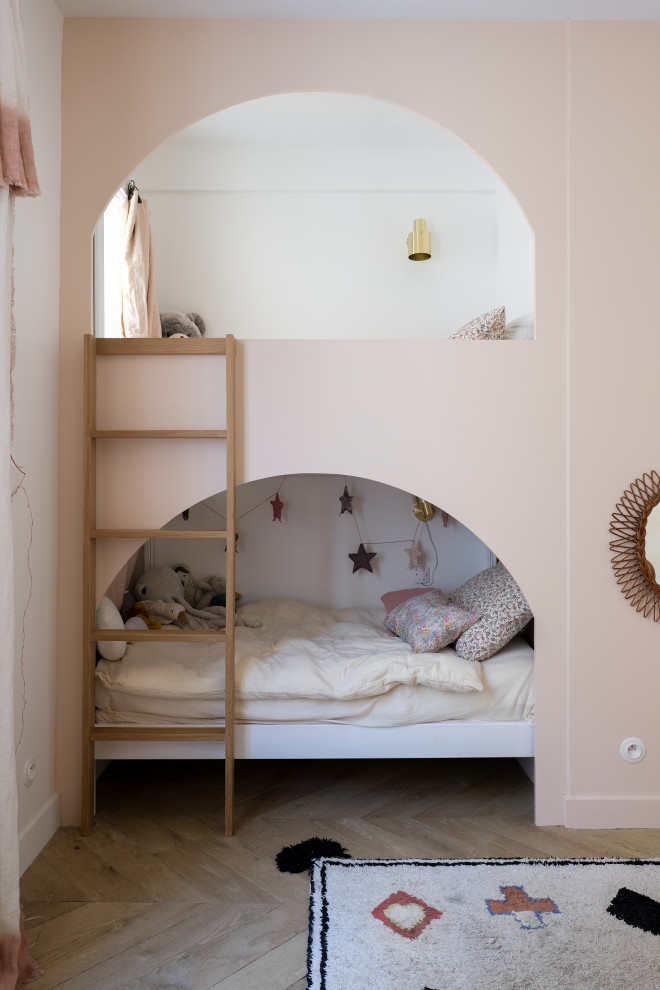 This is an example of a contemporary kids' bedroom for girls in Paris with pink walls, medium hardwood flooring and brown floors.