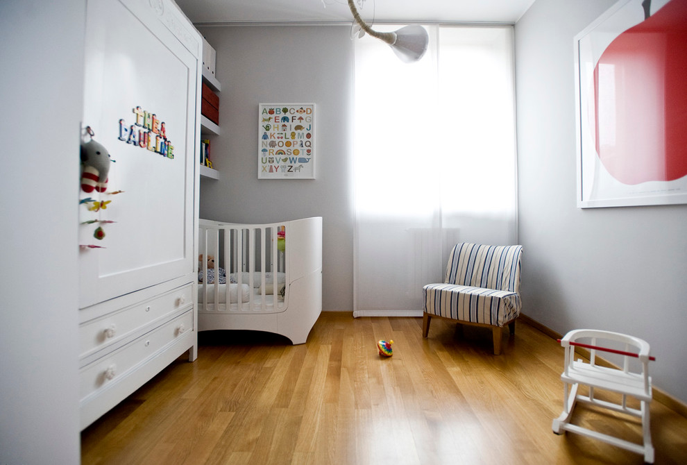 Immagine di una piccola cameretta per neonati design con pareti grigie e parquet chiaro