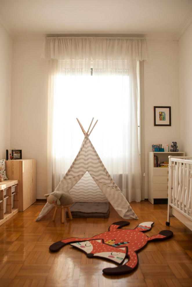 This is an example of a medium sized scandinavian gender neutral nursery in Milan with white walls, light hardwood flooring and brown floors.