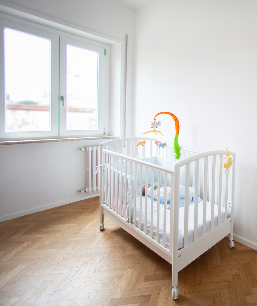 Foto på ett litet funkis könsneutralt babyrum, med vita väggar och ljust trägolv