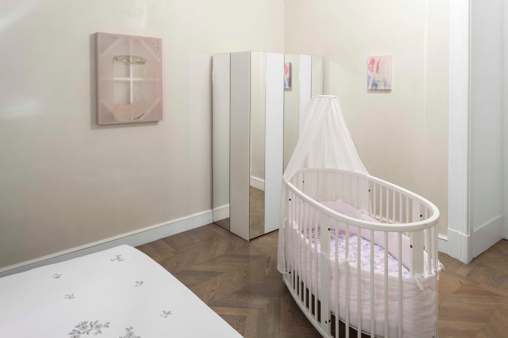 Modelo de habitación de bebé niña actual extra grande con paredes beige y suelo de madera en tonos medios