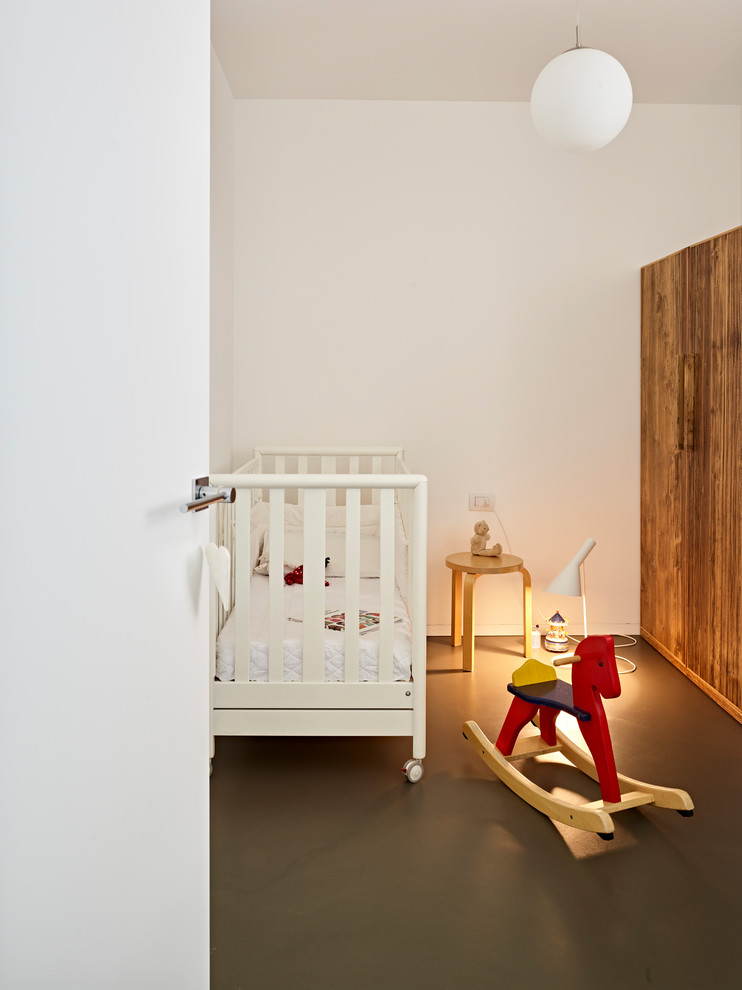 Modelo de habitación de bebé neutra contemporánea de tamaño medio con paredes blancas, suelo de cemento y suelo negro