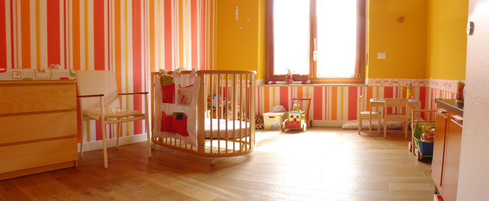 Réalisation d'une grande chambre de bébé fille minimaliste avec un mur multicolore et un sol en bois brun.