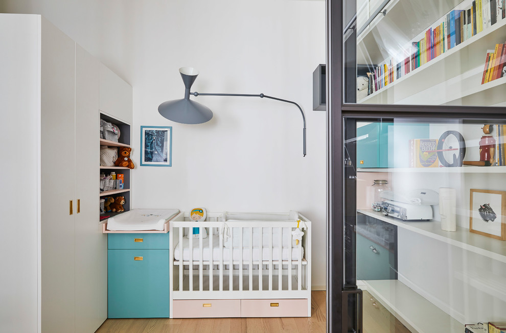 Medium sized contemporary gender neutral nursery in Milan with white walls, light hardwood flooring, beige floors and feature lighting.