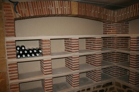 Cette image montre une petite cave à vin traditionnelle avec un sol en brique, des casiers et un sol rouge.