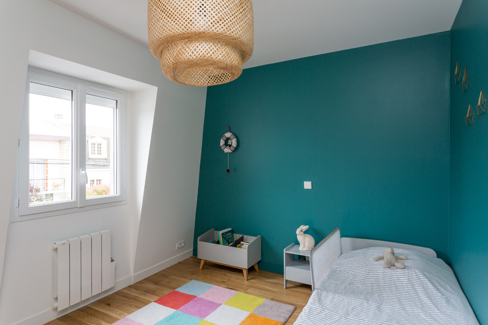 Klassisk inredning av ett mellanstort könsneutralt barnrum kombinerat med sovrum och för 4-10-åringar, med blå väggar, ljust trägolv och beiget golv