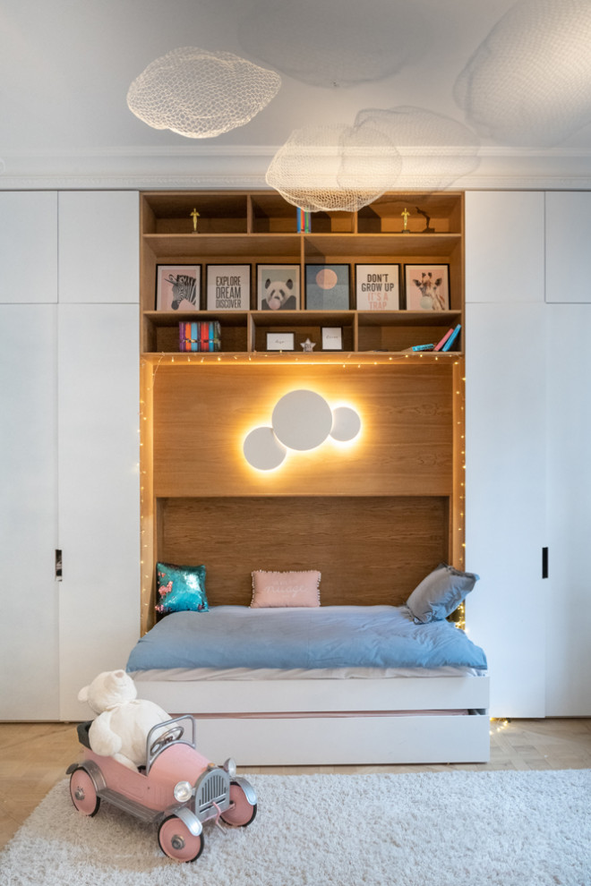 Photo of a medium sized contemporary children’s room for girls in London with white walls, light hardwood flooring and beige floors.