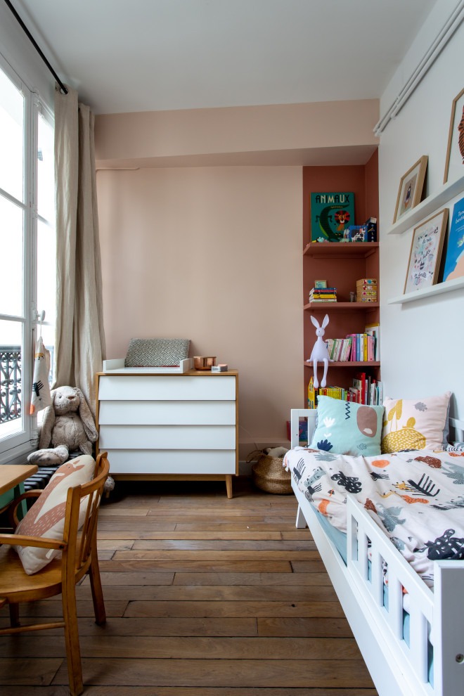 Ispirazione per una cameretta per bambini da 1 a 3 anni moderna di medie dimensioni con pareti rosa e pavimento in legno massello medio