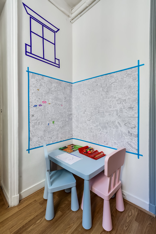 Exempel på ett litet modernt könsneutralt småbarnsrum kombinerat med skrivbord, med vita väggar och mellanmörkt trägolv