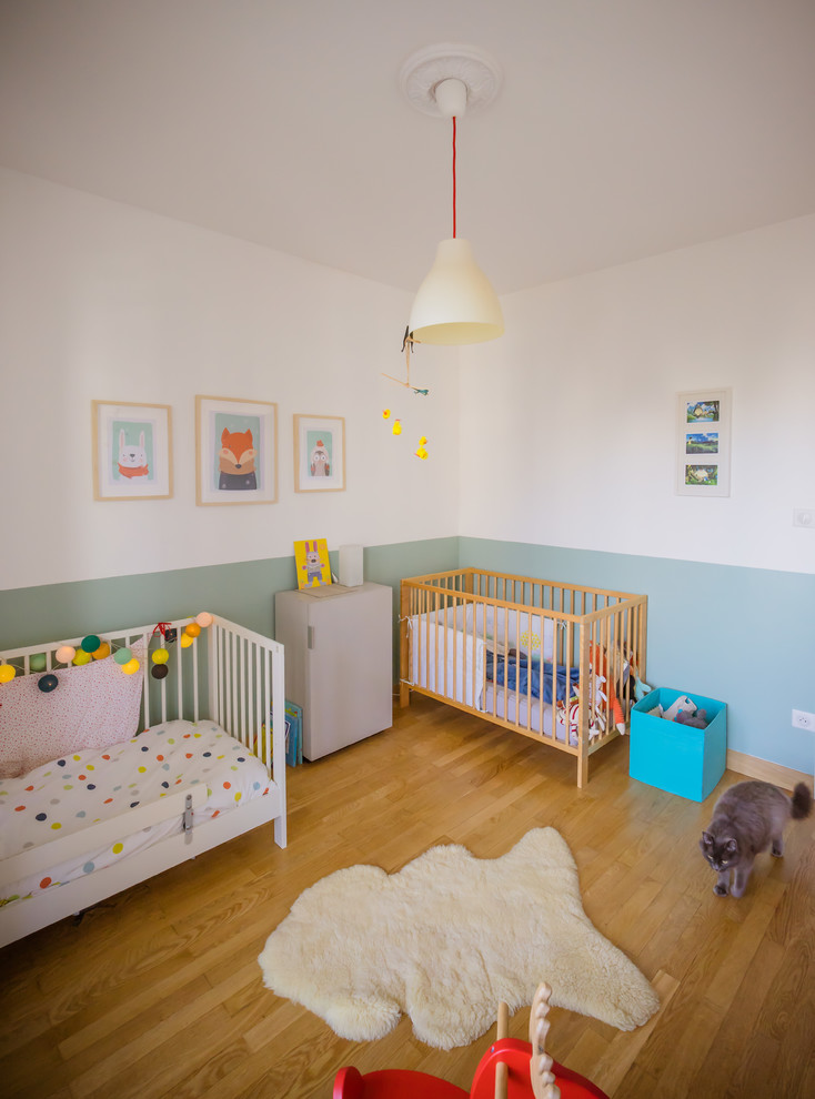 This is an example of a medium sized contemporary gender neutral toddler’s room in Lyon with green walls and light hardwood flooring.