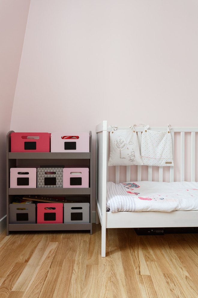 Esempio di una cameretta per bambini da 1 a 3 anni moderna di medie dimensioni con pareti rosa, pavimento in legno massello medio e pavimento beige