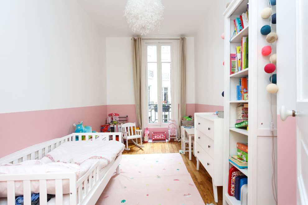 На фото: детская среднего размера в скандинавском стиле с спальным местом, паркетным полом среднего тона, розовыми стенами и коричневым полом для ребенка от 1 до 3 лет, девочки с