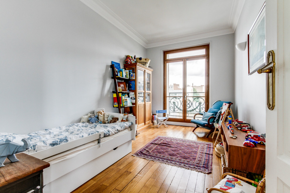 Inredning av ett klassiskt mellanstort barnrum kombinerat med sovrum, med blå väggar, ljust trägolv och beiget golv