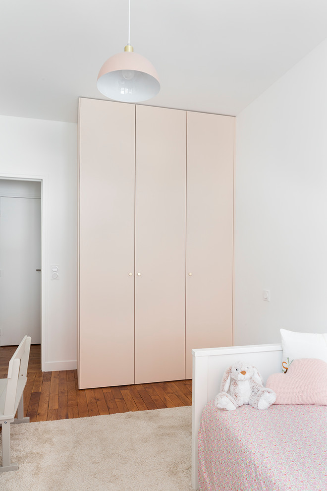 Cette photo montre une chambre d'enfant de 1 à 3 ans tendance de taille moyenne avec un mur rose et un sol en bois brun.