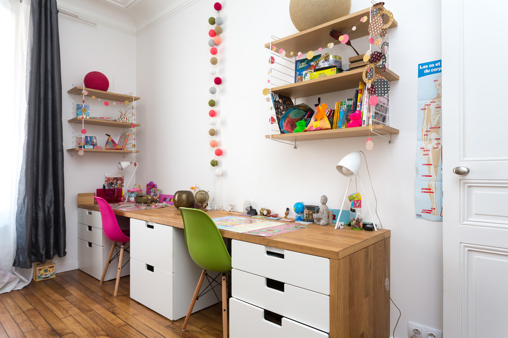 Foto på ett funkis könsneutralt barnrum kombinerat med skrivbord, med vita väggar, mellanmörkt trägolv och brunt golv