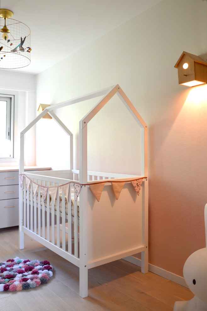 Aménagement d'une chambre de bébé romantique avec un mur rose et parquet clair.