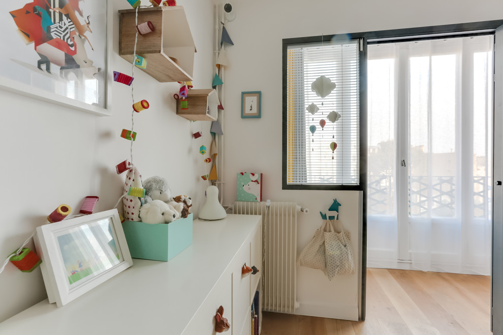 Small contemporary nursery for boys in Paris with white walls and light hardwood flooring.