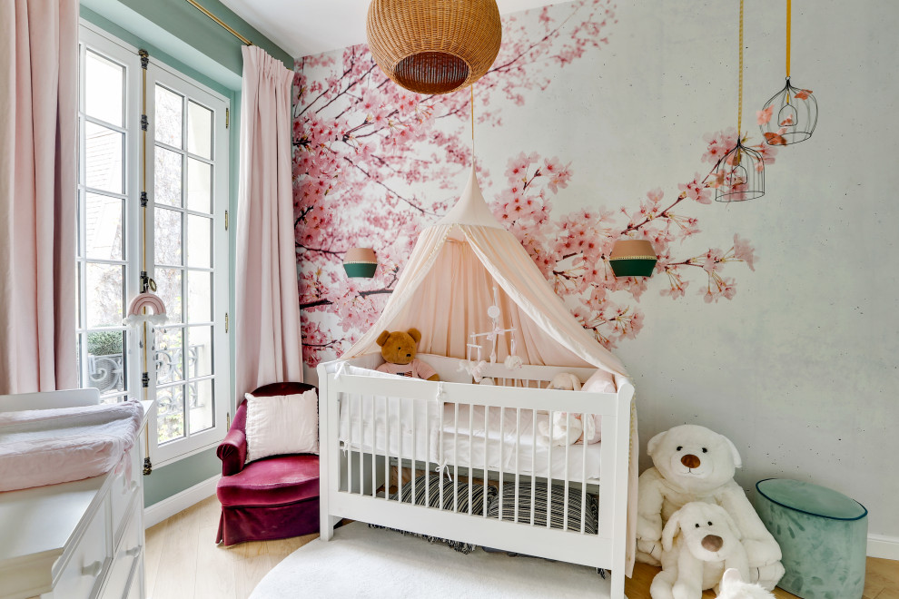 Modelo de habitación de bebé contemporánea con paredes multicolor, suelo de madera clara, suelo beige y papel pintado