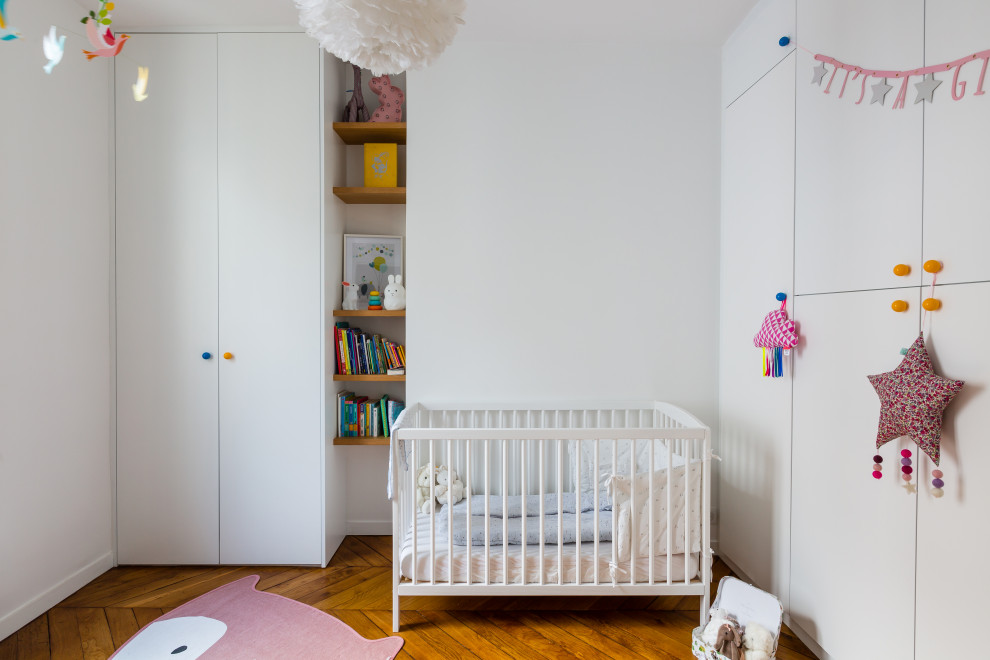 Exemple d'une chambre de bébé fille tendance avec un mur blanc, un sol en bois brun et un sol marron.