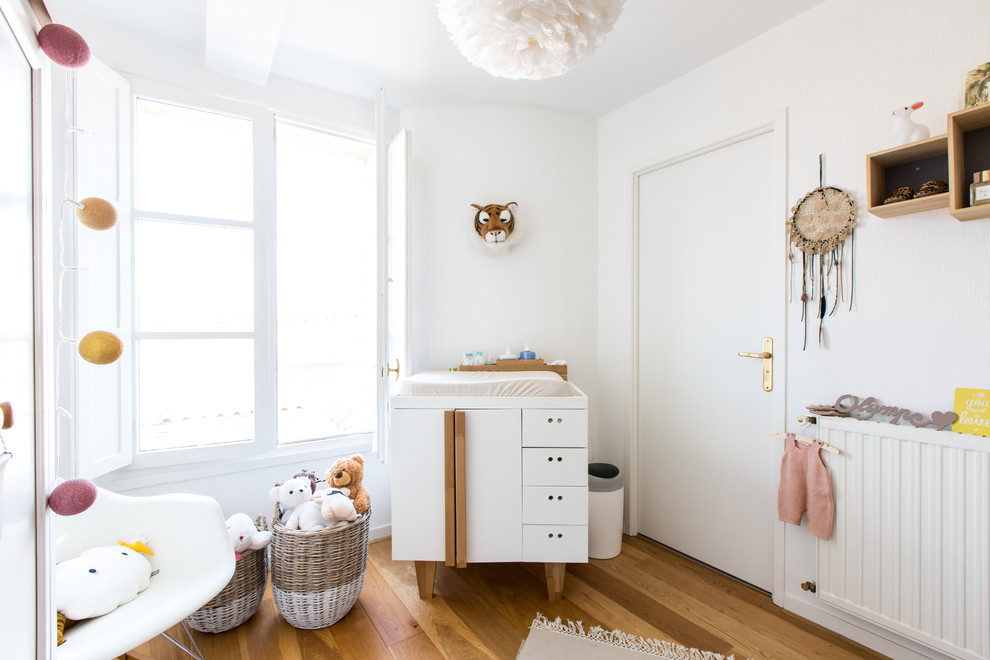Aménagement d'une chambre de bébé fille scandinave avec un mur blanc, un sol en bois brun et un sol marron.