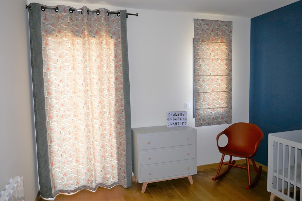 Cette photo montre une chambre de bébé neutre tendance de taille moyenne avec un mur blanc et un sol en bois brun.