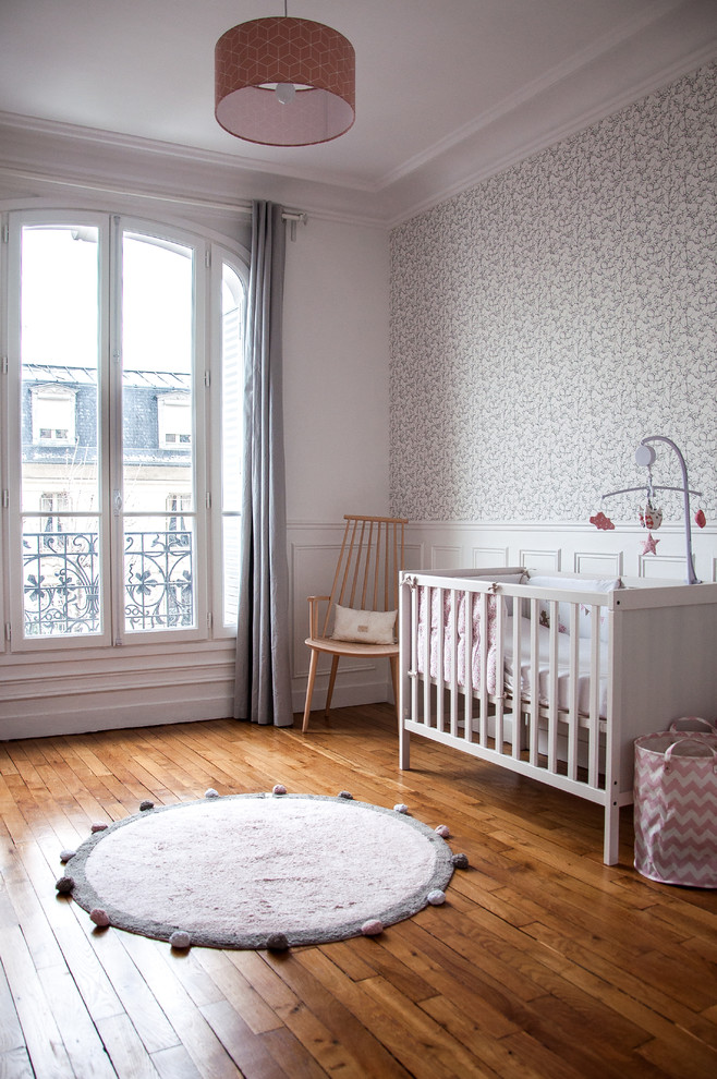 Diseño de habitación de bebé niña escandinava con paredes blancas, suelo de madera oscura y suelo marrón