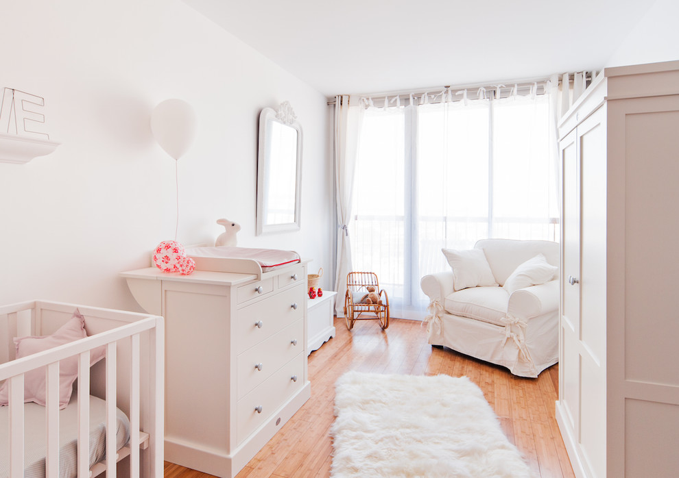Imagen de habitación de bebé neutra tradicional grande con paredes blancas y suelo de madera en tonos medios