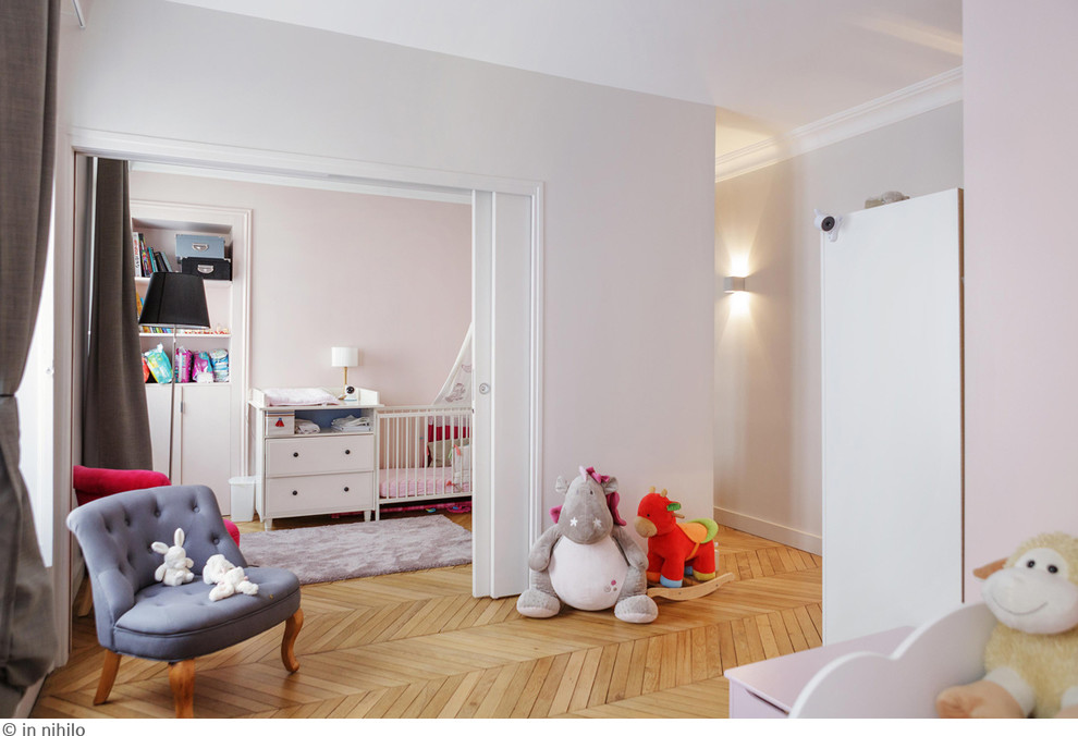 Ejemplo de habitación de bebé neutra contemporánea de tamaño medio con suelo de madera clara, paredes rosas y suelo beige