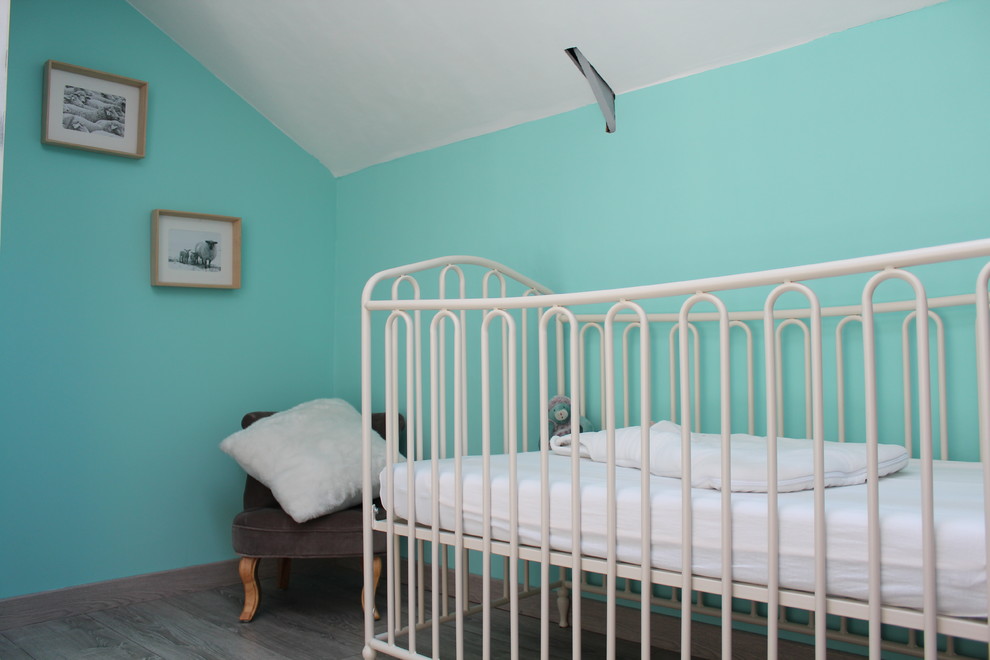 Diseño de habitación de bebé neutra de estilo de casa de campo de tamaño medio con suelo de madera clara y paredes azules