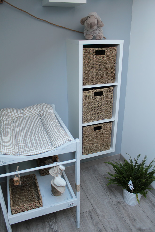 Ejemplo de habitación de bebé neutra de estilo de casa de campo de tamaño medio con paredes azules y suelo de madera clara