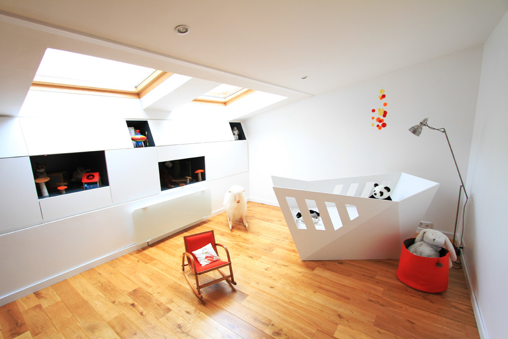 Idées déco pour une chambre de bébé neutre contemporaine de taille moyenne avec un mur blanc et un sol en bois brun.