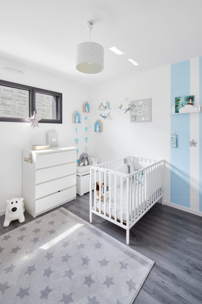 Diseño de habitación de bebé niño actual de tamaño medio con paredes azules, suelo laminado y suelo gris