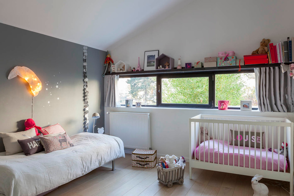 Imagen de habitación de bebé niña urbana de tamaño medio con paredes blancas, suelo de contrachapado y suelo beige