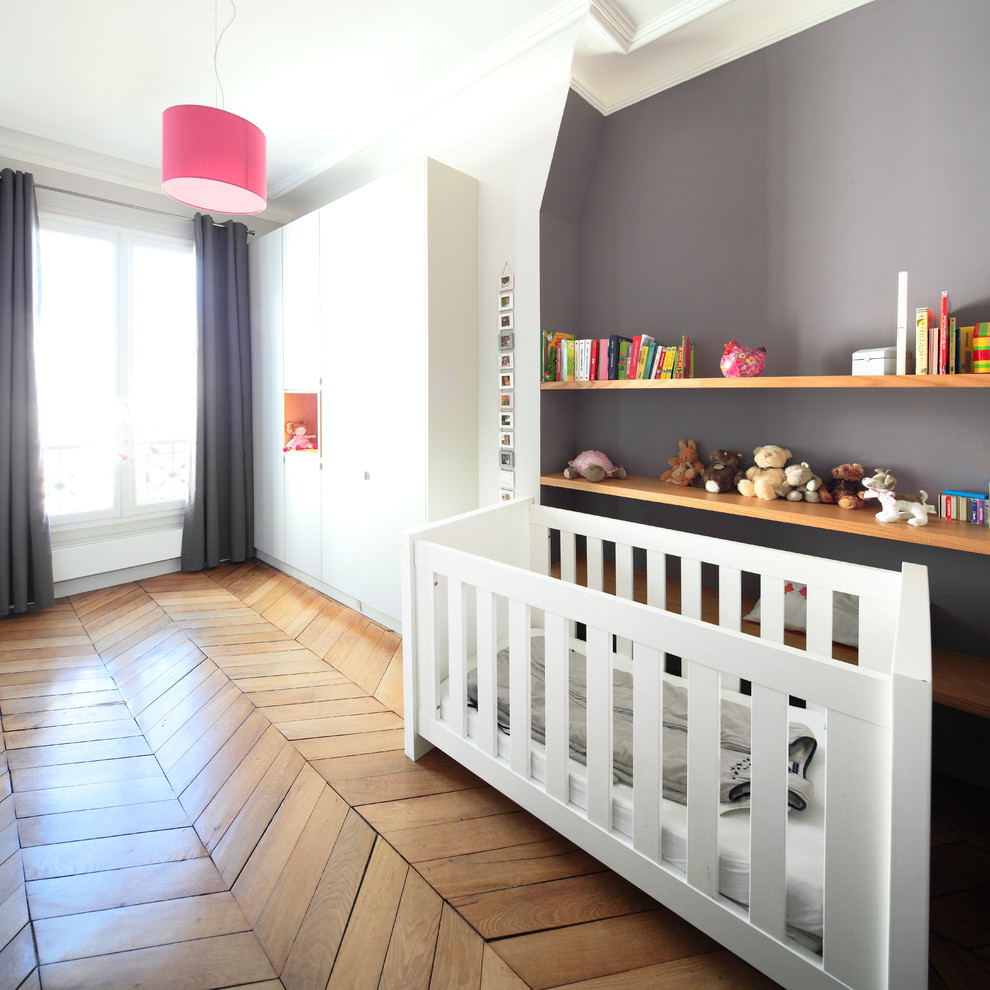 Cette image montre une grande chambre de bébé neutre design avec un mur gris et parquet clair.