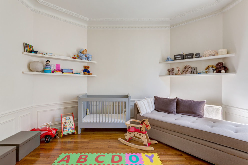 Diseño de habitación de bebé neutra tradicional grande con paredes blancas y suelo de madera en tonos medios