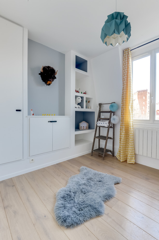 Photo of a modern nursery for boys in Paris with blue walls and light hardwood flooring.