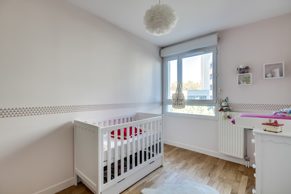 Imagen de habitación de bebé neutra minimalista de tamaño medio con paredes rosas y suelo de madera clara