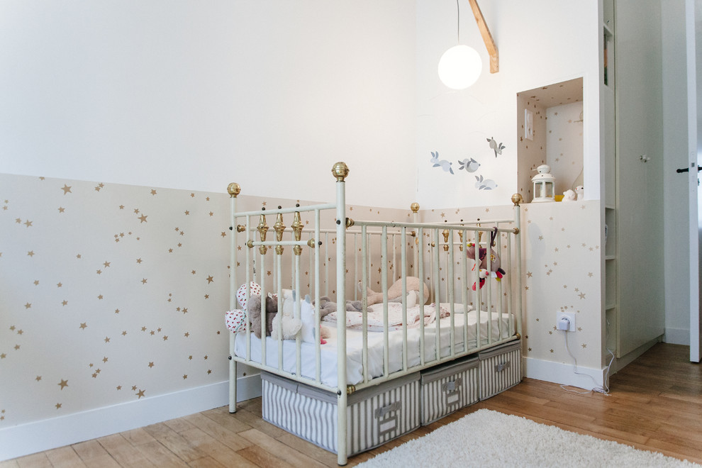 Cette image montre une chambre de bébé neutre nordique de taille moyenne avec un mur blanc et un sol en bois brun.