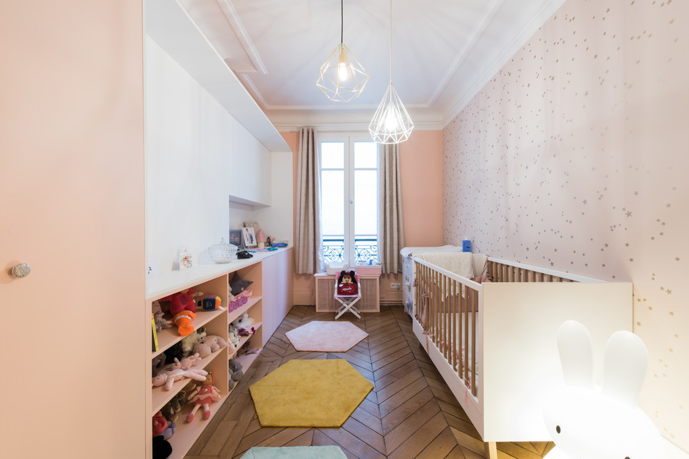 На фото: комната для малыша среднего размера в скандинавском стиле с розовыми стенами, паркетным полом среднего тона и коричневым полом для девочки с