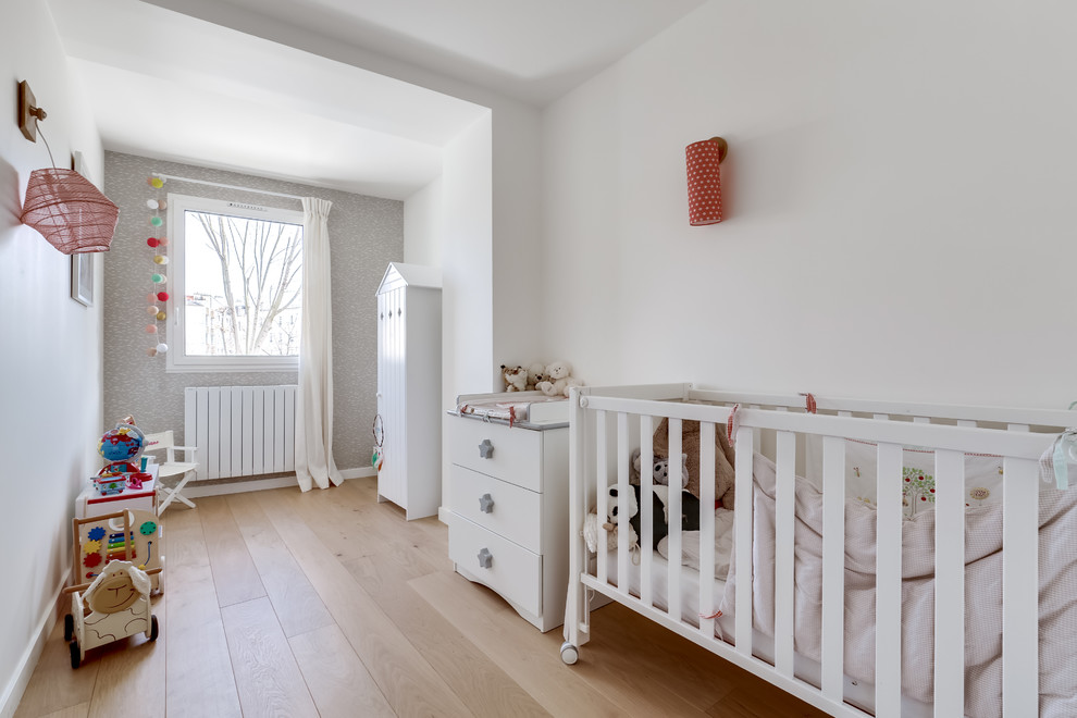 Imagen de habitación de bebé actual con paredes blancas, suelo de madera clara y suelo beige