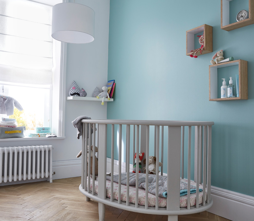 Modelo de habitación de bebé niño contemporánea de tamaño medio con paredes azules y suelo de madera en tonos medios