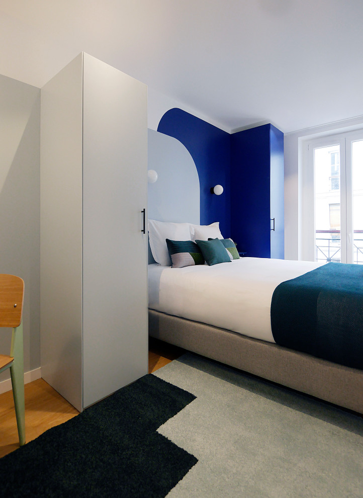 Modelo de dormitorio actual de tamaño medio con paredes multicolor, suelo de madera en tonos medios, suelo marrón y papel pintado