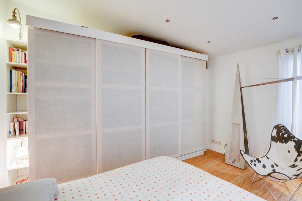 Idée de décoration pour une chambre parentale design de taille moyenne avec un mur blanc, parquet clair, aucune cheminée et un sol marron.